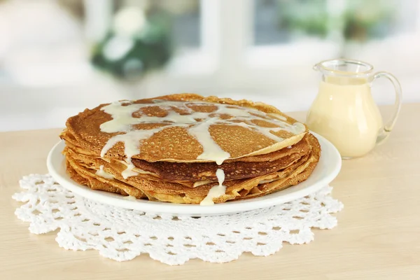 Sweet pancakes on plate with condensed milk on table in kitchen — Stock Photo, Image