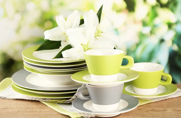 Prázdné talíře a poháry na dřevěný stůl na zeleném pozadí — Stock fotografie