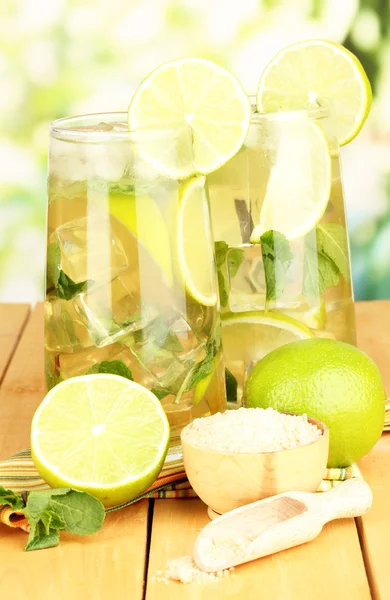 Bicchieri di cocktail con lime e menta su tavolo di legno su sfondo brillante — Foto Stock