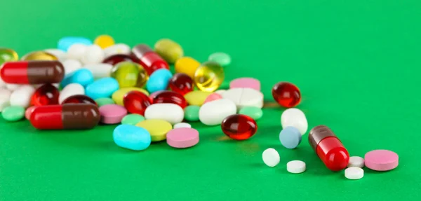 Surtido de pastillas, tabletas y cápsulas sobre fondo verde — Foto de Stock