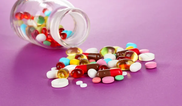 Prášky, tablety a kapsle na fialovém pozadí — Stock fotografie