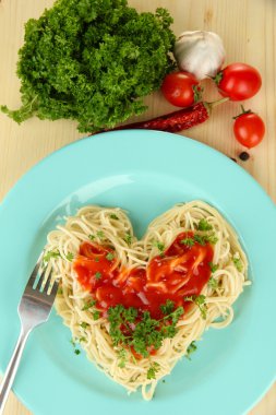 Cooked spaghetti carefully arranged in heart shape and topped with tomato sauce, on wooden background