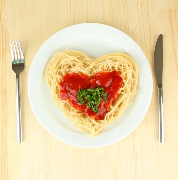 Готовые спагетти тщательно расположены в форме сердца и увенчаны томатным соусом, на деревянном фоне — стоковое фото