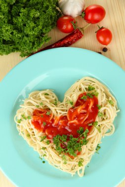 Cooked spaghetti carefully arranged in heart shape and topped with tomato sauce, on wooden background