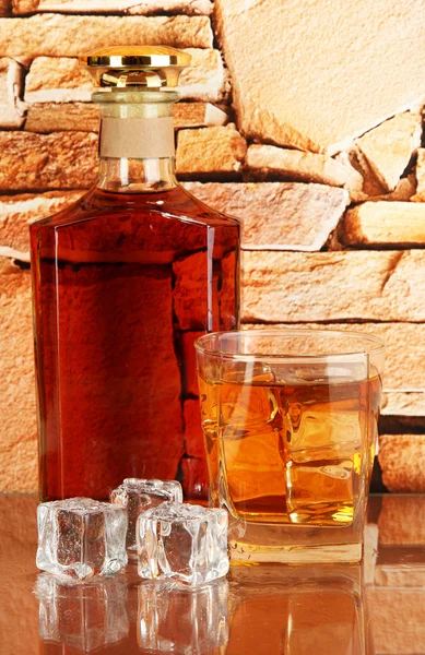 Бутылка и стакан виски и льда на фоне кирпичной стены — стоковое фото