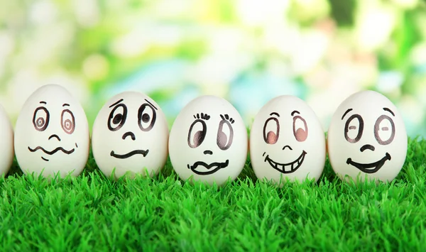 Ovos com rostos engraçados na grama no fundo brilhante — Fotografia de Stock