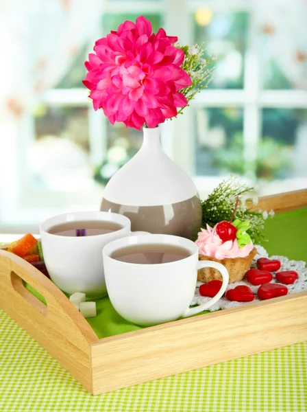 Cups of tea with flower and cake on wooden tray on table in room — Stock Photo, Image