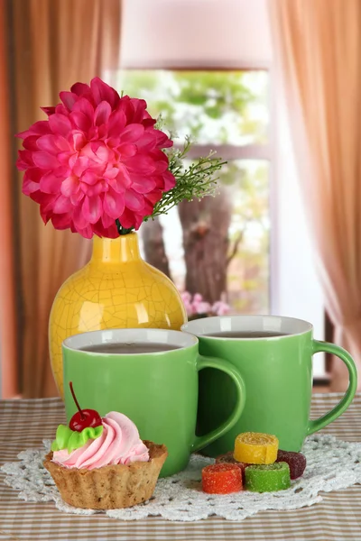 Tassen Tee mit Kuchen, Süßigkeiten und Blumen auf dem Tisch im Zimmer — Stockfoto