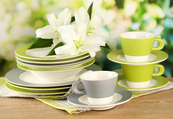 Empty plates and cups on wooden table on green background — Stock Photo, Image