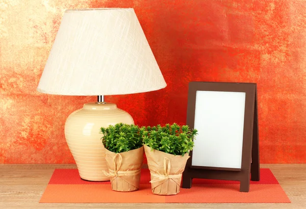 Brown photo frame and lamp on wooden table on red wall background — Stock Photo, Image