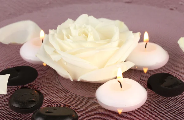 Piedras de spa con flores y velas en agua en el plato —  Fotos de Stock