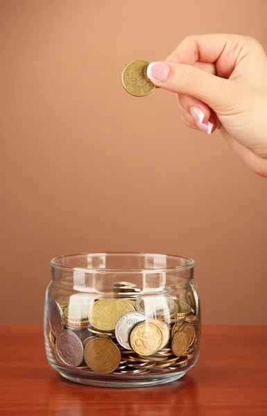 Εξοικονόμηση, γυναικείο χέρι θέση ένα κέρμα σε γυάλινο μπουκάλι, σε φόντο χρώμα — Φωτογραφία Αρχείου