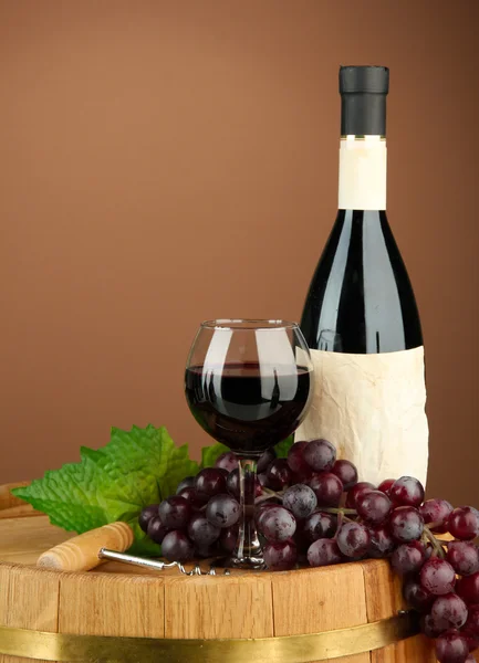 Composition of wine bottle, glass and grape,on wooden barrel, on brown background — Stock Photo, Image