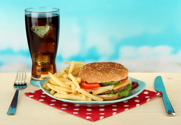 Tasty cheeseburger with fried potatoes and cold drink, on bright background — Stock Photo, Image