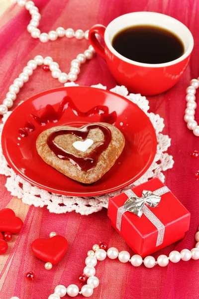 Chocolate cookie in form of heart with cup of coffee on pink tablecloth close-up — Stock Photo, Image