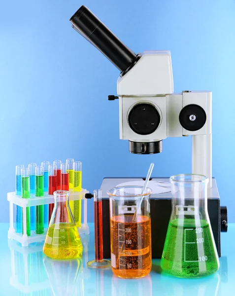 Test tubes with colorful liquids and microscope on blue background — Stock Photo, Image