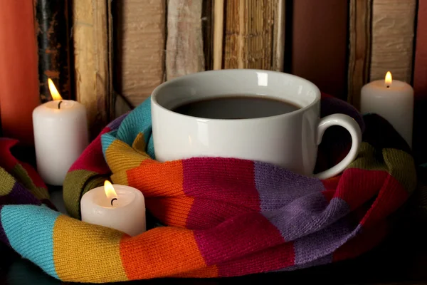 Cup of coffee wrapped in scarf on books background — Stock Photo, Image