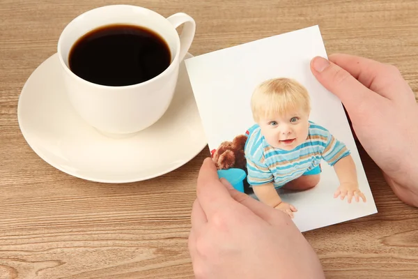Photo in hands and cup of coffee on wooden table — Stock Photo, Image