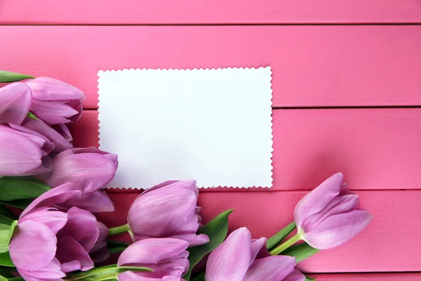 Vacker bukett lila tulpaner och tomma kort på rosa trä bakgrund — Stockfoto