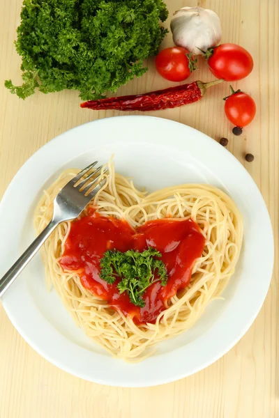 Gotowane spaghetti starannie ułożone w kształcie serca i polane sosem pomidorowym, na tle drewniane — Zdjęcie stockowe