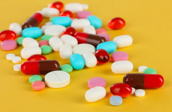 Assortment of pills, tablets and capsules on yellow background — Stock Photo, Image