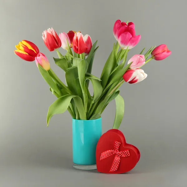 Schöne Tulpen im Eimer mit Geschenken auf grauem Hintergrund — Stockfoto