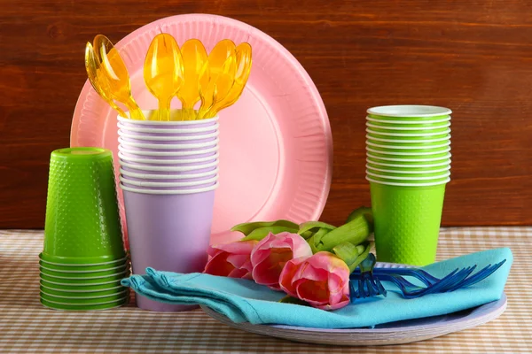 Louça de mesa de plástico multicolorido na mesa com tulipas em fundo de madeira — Fotografia de Stock