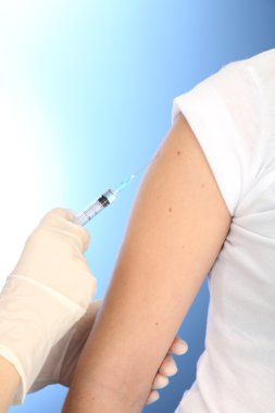 Doktor holding şırınga ile hasta omzundan, mavi zemin üzerine aşı