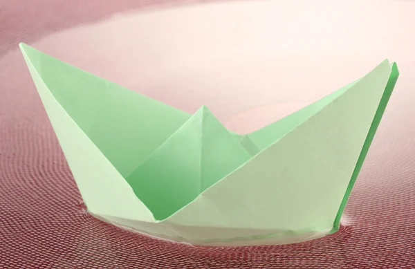 Barco de papel de color en agua en placa rosa, primer plano — Foto de Stock