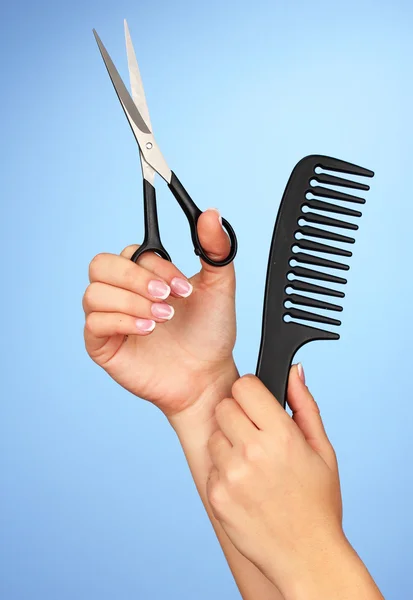 Color comb and scissors in female hand on color background — Stock Photo, Image