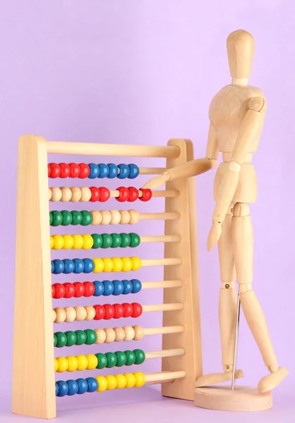 Abacus de brinquedo brilhante e manequim de madeira, no fundo roxo — Fotografia de Stock