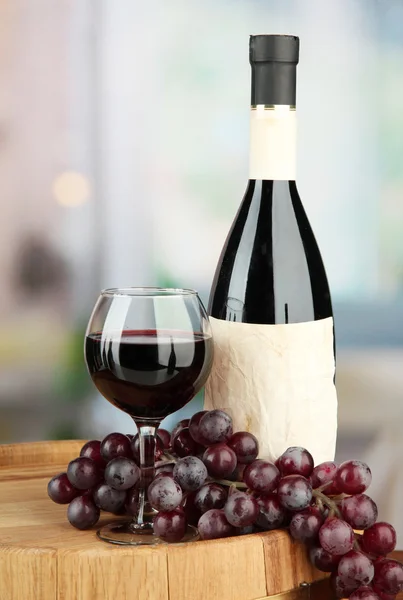 Composição de garrafa de vinho, vidro e uva, em barril de madeira, sobre fundo brilhante — Fotografia de Stock