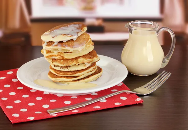 Söta pannkakor på tallrik med kondenserad mjölk på bordet i rummet — Stockfoto