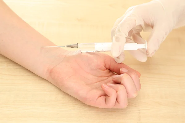 Médico sosteniendo la jeringa con una vacuna en la mano del paciente, sobre fondo de madera — Foto de Stock