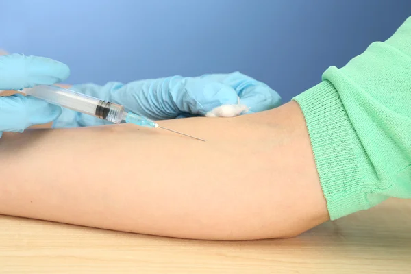 Doktor hastanın el, mavi zemin üzerine aşı holding şırınga — Stok fotoğraf