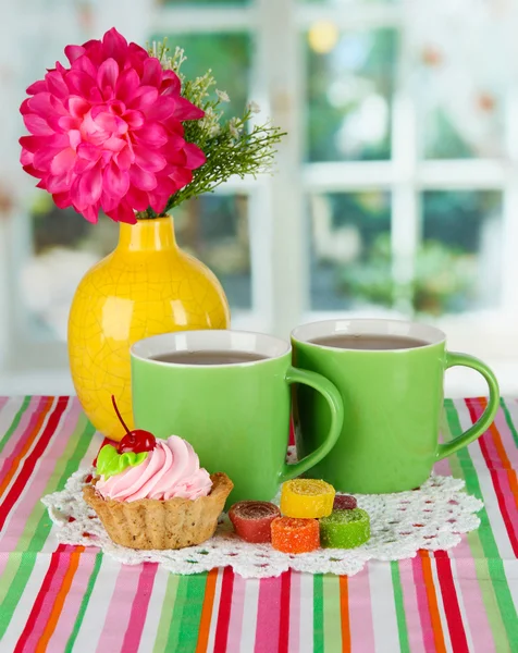 Cups of tea with cake,candy and flower on table in room — Stock Photo, Image
