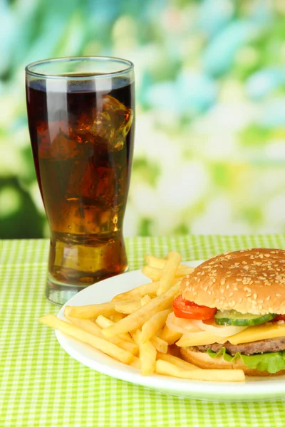 Tasty cheeseburger with fried potatoes and cold drink, on bright background — Stock Photo, Image