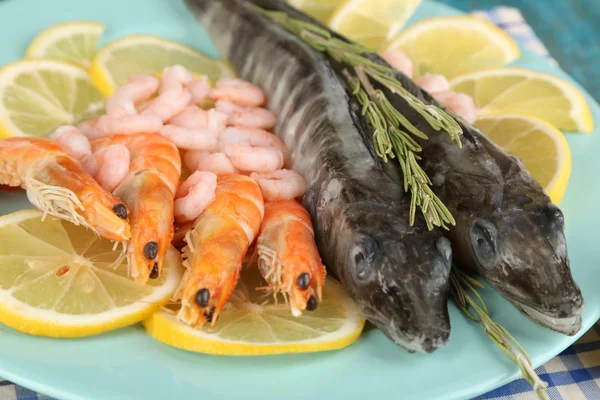 Peces frescos con camarones y limón en plato sobre mesa de madera de cerca — Foto de Stock