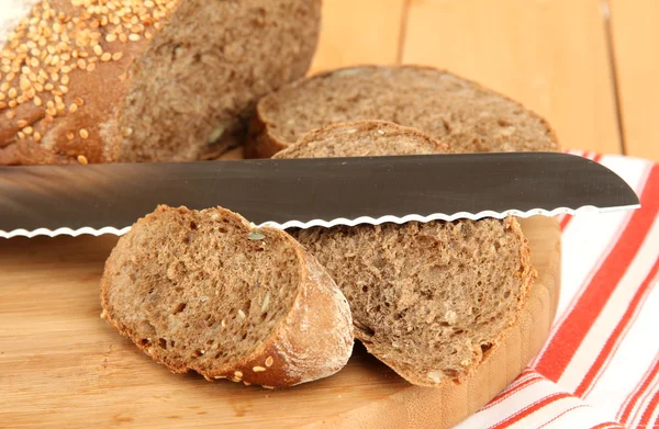 Pan rebanado con semillas de sésamo y cuchillo en tabla de cortar sobre mesa de madera de cerca — Foto de Stock
