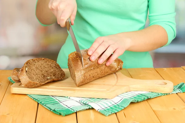 Woman slicing bread with sesame seeds on chopping board on wooden table close up — Stock Photo, Image