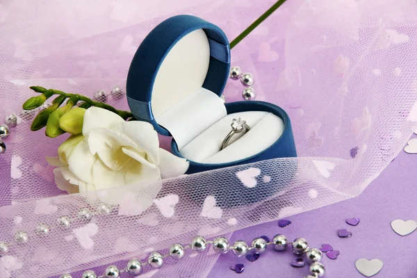Schöne Schachtel mit Ehering und Blume auf lila Hintergrund Stockbild