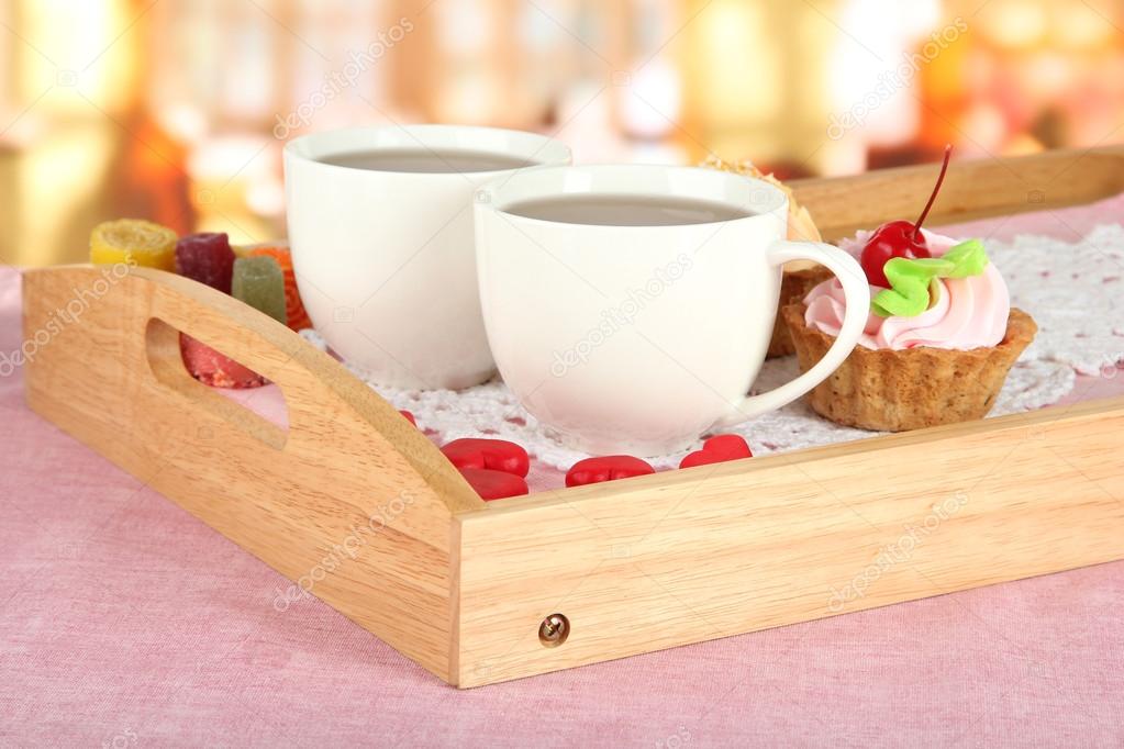 Cups of tea with cakes on wooden tray on table in cafe