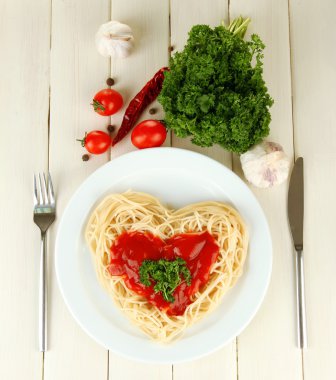 Cooked spaghetti carefully arranged in heart shape and topped with tomato sauce, on wooden background