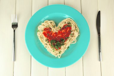 Cooked spaghetti carefully arranged in heart shape and topped with tomato sauce, on wooden background