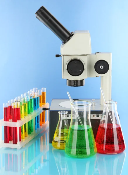 Provette con liquidi colorati e microscopio su fondo blu — Foto Stock