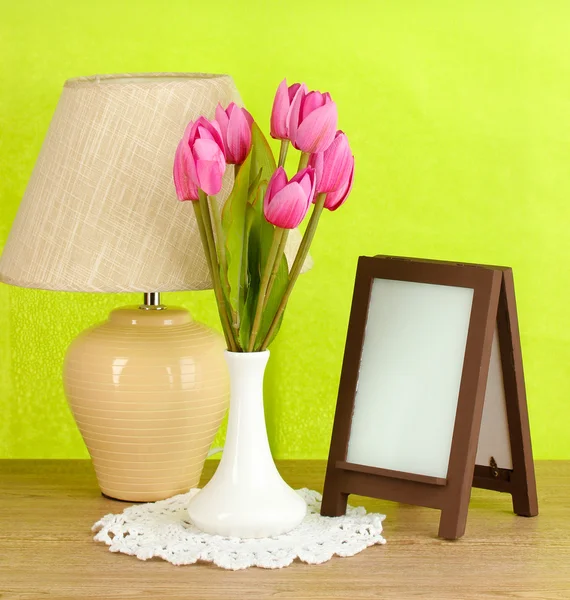 Marco de fotos marrón y lámpara sobre mesa de madera sobre fondo de pared verde —  Fotos de Stock