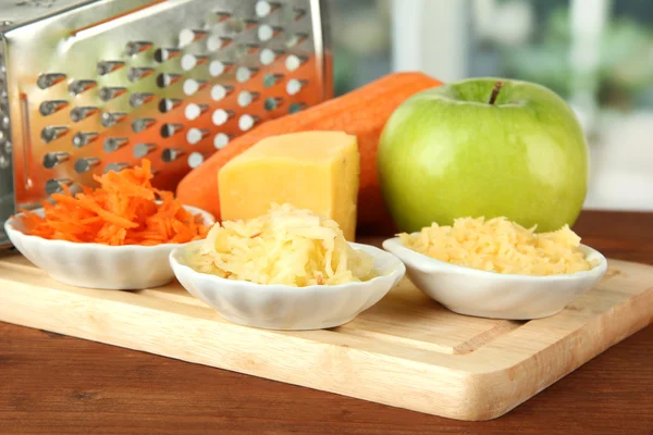 Metal grater and apple, cheese, carrot, on cutting board, on bright background — Stock Photo, Image