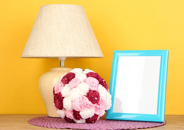 Marco de fotos colorido, lámpara y flores en la mesa de madera sobre fondo amarillo — Foto de Stock