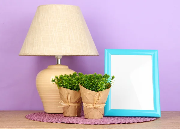 Marco de fotos colorido, lámpara y flores en la mesa de madera sobre fondo lila — Foto de Stock