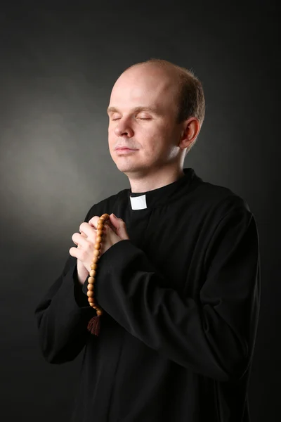 Священник с четками на черном фоне — стоковое фото